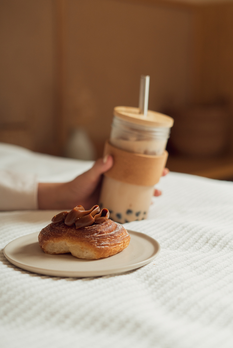 Person's Hand Holding Milk Tea Near a Sweet Bread